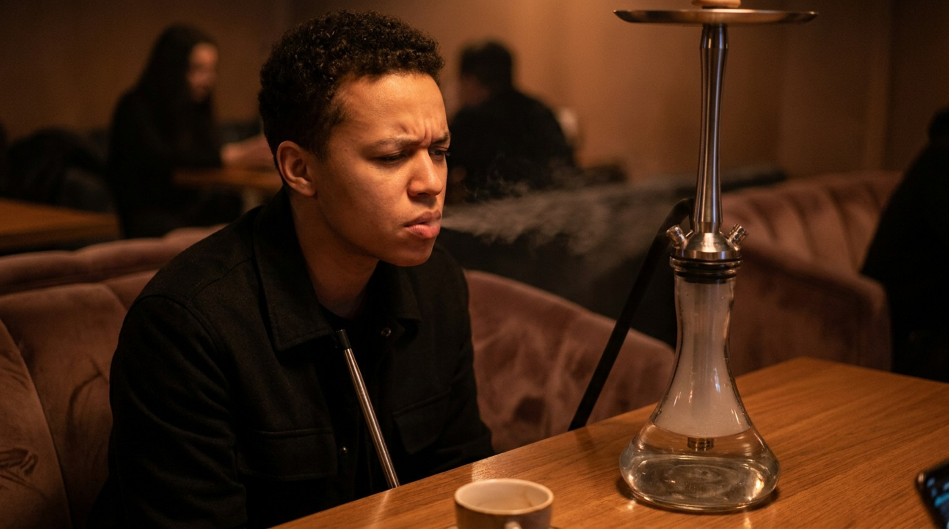 Man examining a hookah while smoke escapes around the glass base in a lounge.