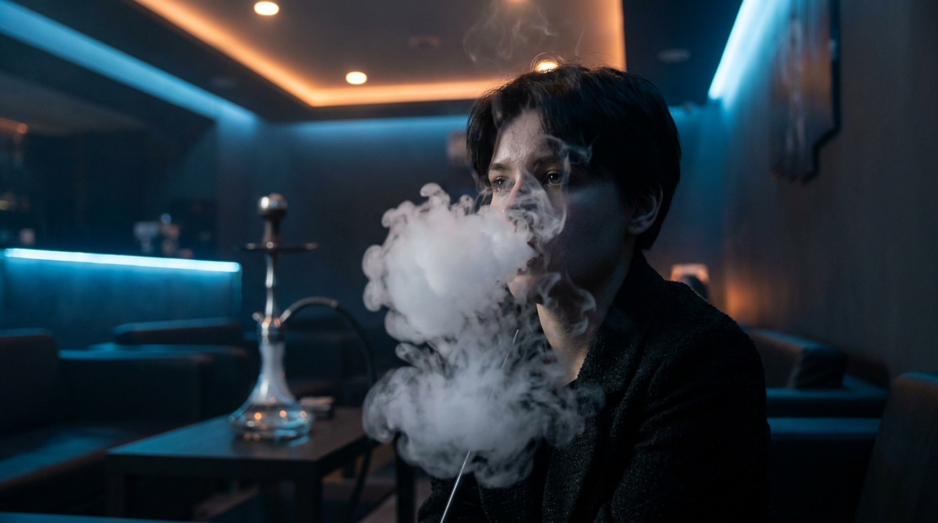 Man exhaling a dense cloud of hookah smoke in a dimly lit lounge.